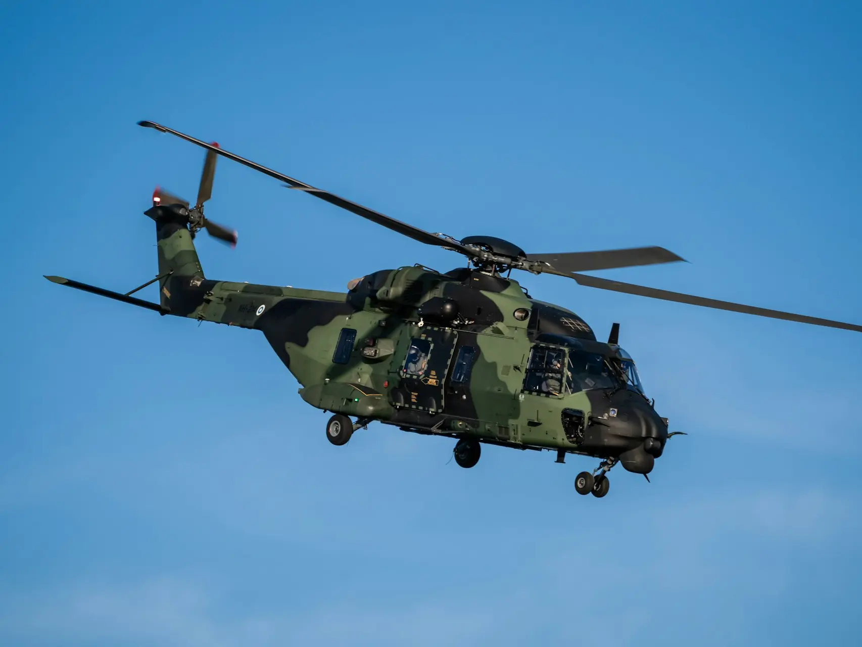 a military helicopter flying through a blue sky