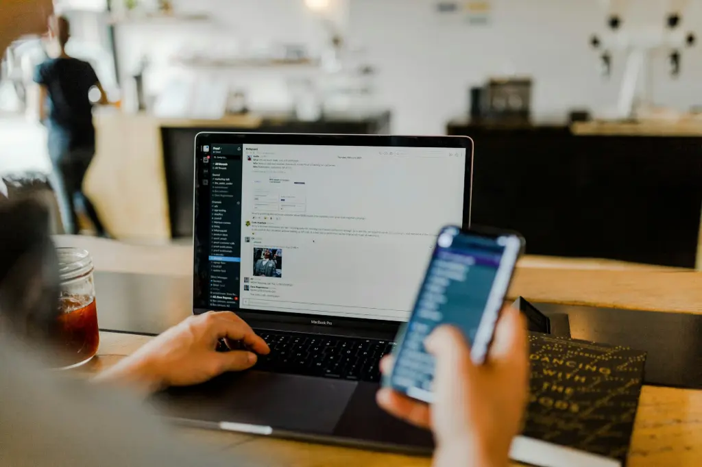 Person using a laptop and smartphone simultaneously in a café, illustrating secure multitasking in a protected network environment